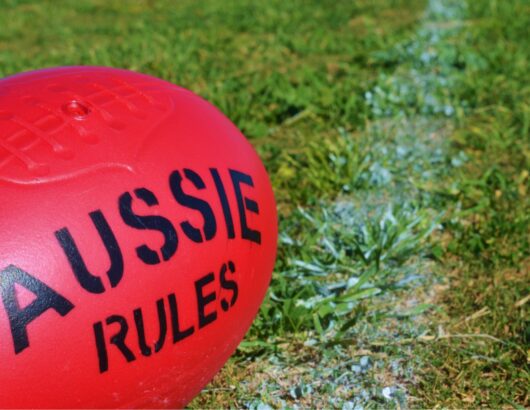 Red rugby ball with the text Aussie Rules on a grass field