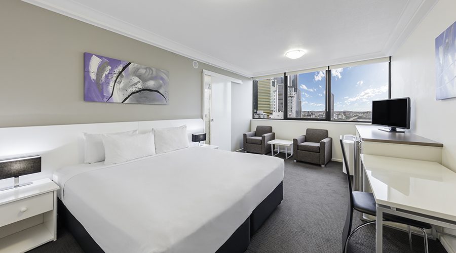 Modern hotel room with a king-sized bed, a work desk, and a sitting area with two armchairs.